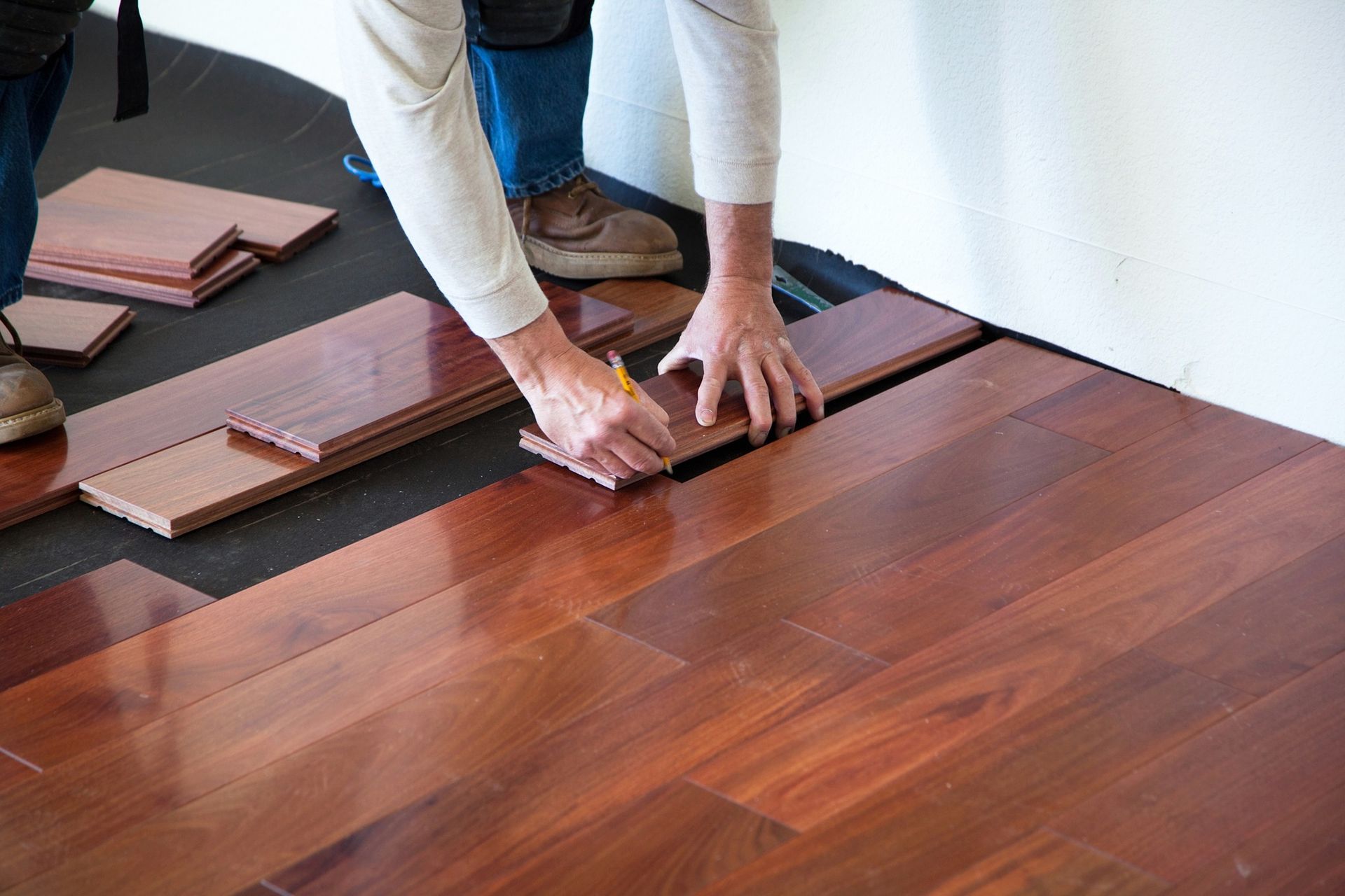 Anonymous hands marking a wood plank with a pencil before fitting it into the floor